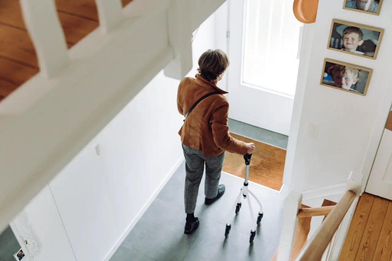 Ältere Frau mit Gehstock oben an der Treppe im eigenen Haus